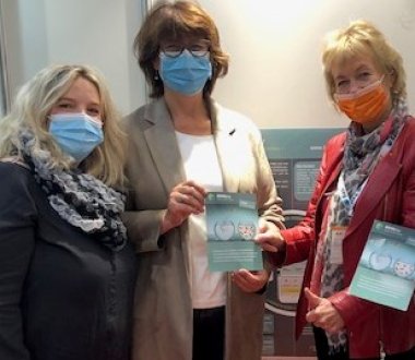 Es sind drei Frauen zu sehen, die Flyer von BEMpsy halten und in die Kamera lächeln.