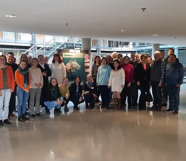 Es ist eine Gruppe von Menschen zu sehen, die in einem Gebäude vor einem Plakat zu BEMpsy stehen.