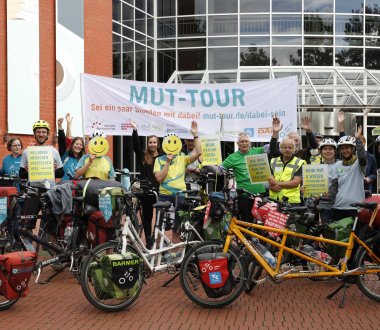 Mehrere Menschen stehen mit Fahrrädern vor der DASA – Arbeitswelt Ausstellung. Sie halten ein Banner und Schilder. Zwei Personen verdecken ihr Gesicht mit Smileys.