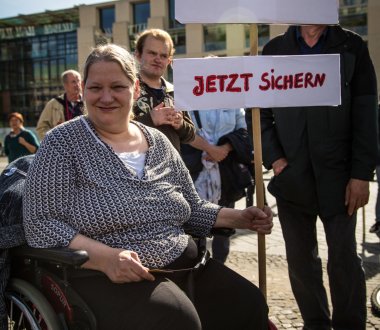 Eine Person sitzt in einem Rollstuhl und hält ein Protestschild, auf dem "Recht auf Teilhabe. Jetzt sichern" steht.