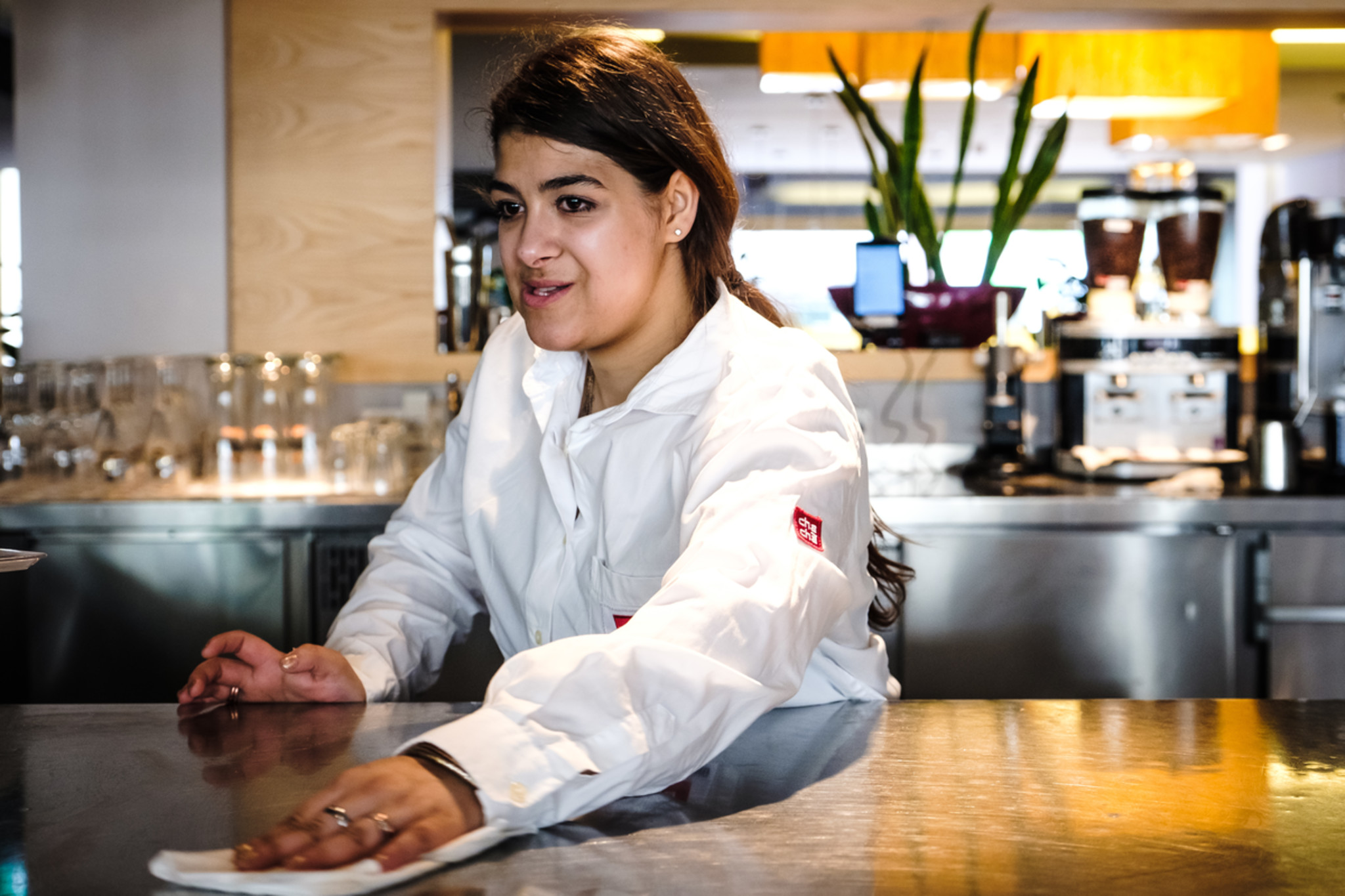 Eine Frau steht in Arbeitskleidung in einem Café und wischt den Tresen mit einem Tuch.