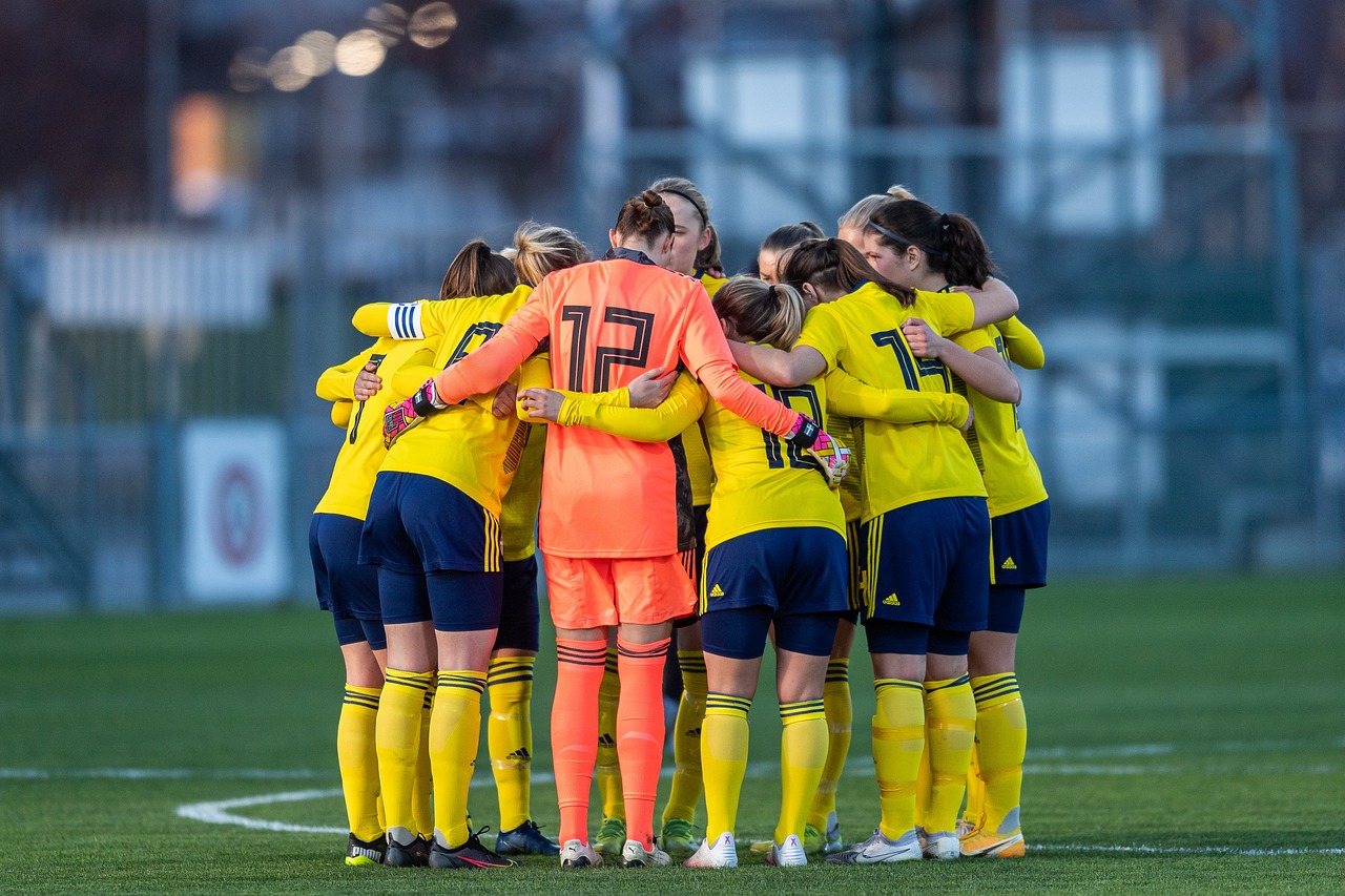 Ein Team von Fußballspieler:innen steht auf einem Feld und umarmt sich im Kreis.